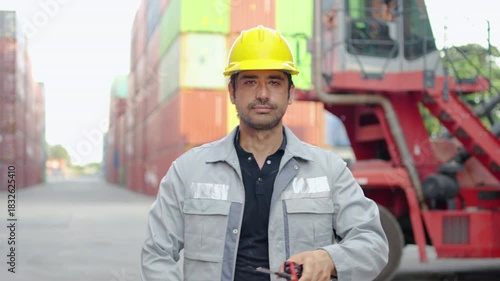 In a bustling container warehouse, engineer worker engages in quality control checks and communicates with colleagues via phone and radio, then looking at camera and smiling confidently.