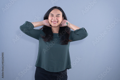 A smiling woman in a dark green top is stretching her neck with hands behind her head