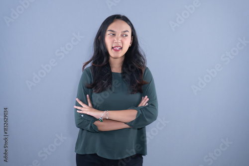 A woman in a green top stands with arms crossed, sticking her tongue out playfully