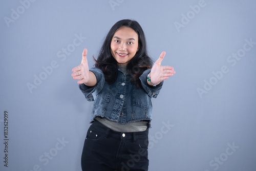 A smiling woman in a denim jacket poses with open arms as if for a hug