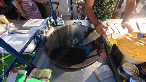 Street Food Prep: An individual, deeply immersed in the craft, expertly crafts a delicious dish on a large, well-worn cooking surface, surrounded by the vibrant energy of a bustling food market. 