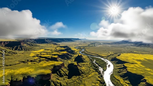 Vast green landscape with river flowing through a canyon under dramatic clouds and bright sunlight