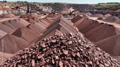 Vast outdoor quarry filled with towering piles of various crushed rock and gravel materials awaiting processing with heavy industrial equipment visible in the background