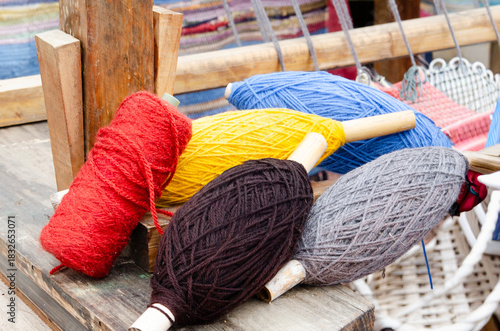 A close-up shot of several spools of colorful yarn, including red, yellow, black, blue, and gray, resting on a rustic wooden surface.