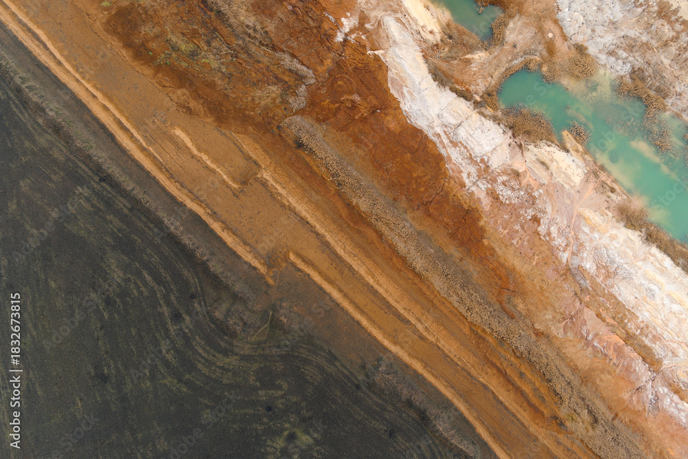 Obraz premium Top-down abstract aerial view of a sharp diagonal contrast between dark tilled soil and multicolored geological quarry layers.