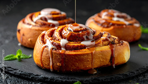 Three Freshly Baked Cinnamon Rolls Drizzled with Sweet Icing on Rustic Slate Surface with Mint Leaves