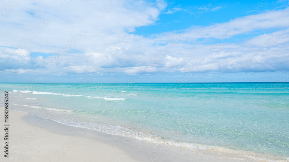 Fototapeta premium Calm ocean waves gently lap on the sandy shore under a bright blue sky