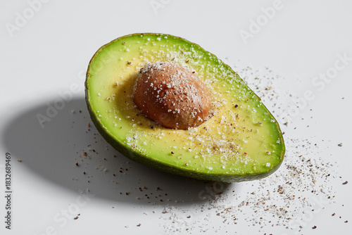 Fresh avocado half sprinkled with salt and pepper, showcasing its vibrant green color and creamy texture, evokes sense of healthy eating and culinary delight