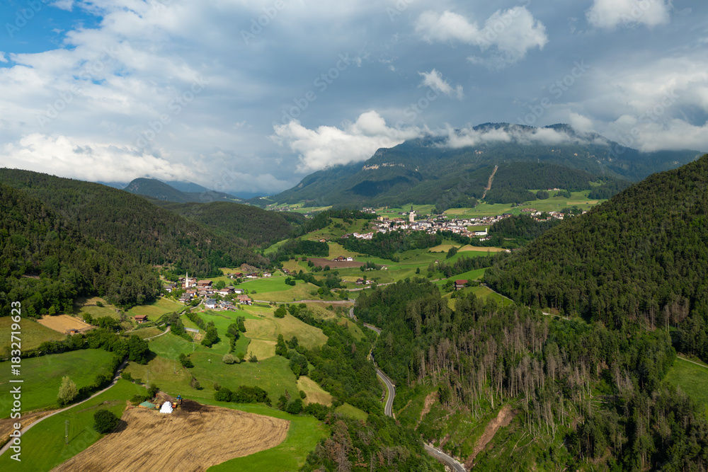 Obraz premium Tisana village with meadows and pasture parcels against mountain ridges, aerial view. Summer alpine landscape in the Dolomites, South Tyrol, Italy.