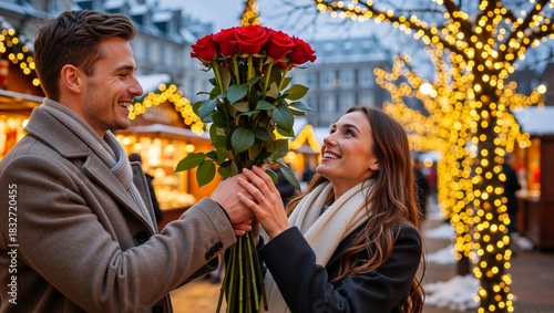 A smiling man gives a large bouquet of red roses to a happy woman. Romantic young couple on a date at a festive winter market with glowing lights