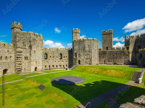 A distinct shadow of castle towers falls across the grassy Inner Ward of Caernarfon Castle (Caernarfon, Wales, United Kingdom)