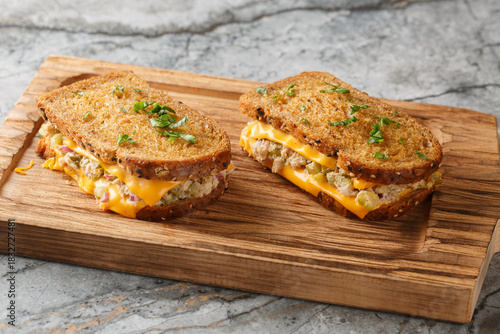 Homemade tuna melt toasts made from buttered bread, canned tuna with vegetables, mayonnaise and melted cheese close-up on a wooden board on the table. Horizontal