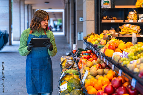 Fotografija Woman grocer managing inventory using tablet at fruit stand