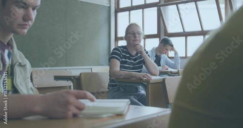 Thinking student wearing glasses and striped tee resting chin at school desk, with notebooks