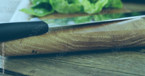 Showing wooden cutting board grain on wooden tabletop, with metal knife black handle and greens