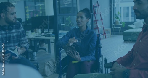 Speaking woman holding tablet and stylus in wheelchair at open-plan office, wearing blue shirt