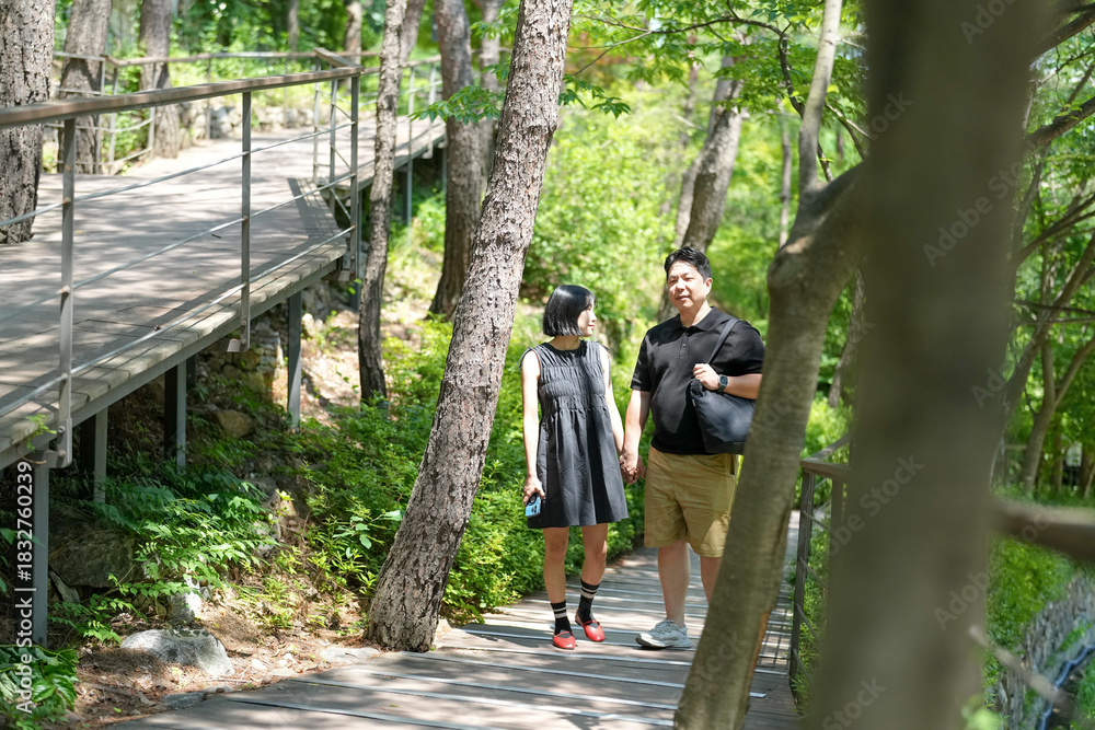 Fototapeta premium A man and woman are walking on a path in a forest. The man is carrying a backpack and the woman is holding his hand. Scene is peaceful and romantic, as the couple enjoys their time together in nature