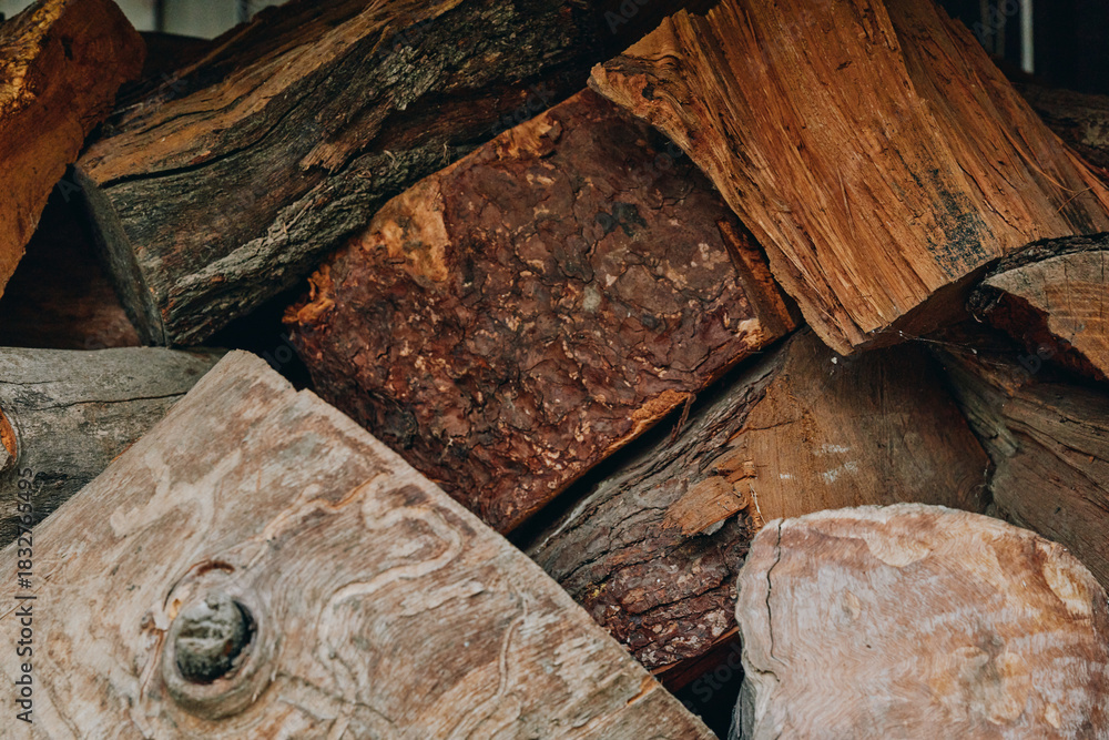 Fototapeta premium Firewood stacked logs woodpile wooden texture rustic split logs bark fuelwood closeup of dried fireplace wood, earthy brown tones and rough wood grain for cabin heating, winter supply and decor.