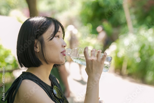 A woman is drinking water from a bottle while sitting on a bench. The scene is peaceful and relaxing, with the woman enjoying a moment of solitude in the outdoors