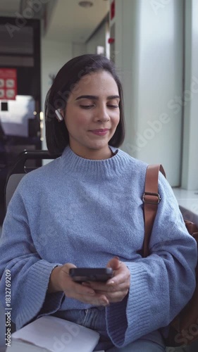 Happy female student using a smartphone and wireless earphones while commuting on a bus or train