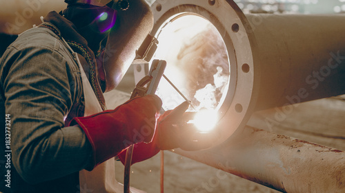 Bild auf Leinwand A worker is engaged in welding an industrial pipe inside a factory