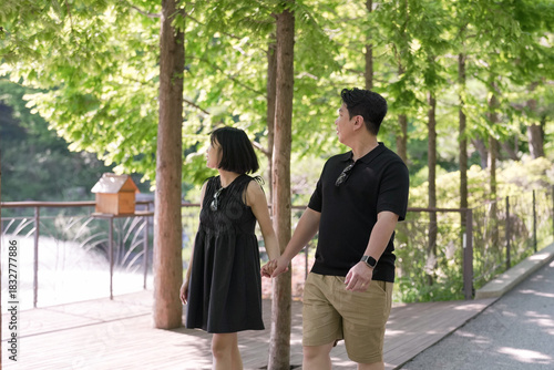 Wallpaper Mural A man and a woman are walking together in a park. The man is wearing a black shirt and the woman is wearing a black dress. They are holding hands and walking under a tree Torontodigital.ca