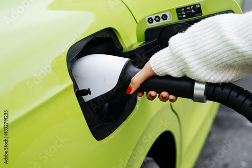 Electric vehicle charging scene captured at an fast-charging station. A person is connecting a bright green car, high-power charger