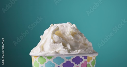 white soft vanilla ice cream in paper cup rotating, food closeup on blue background