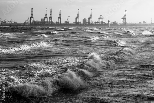 Storm waves surging with Port of Liverpool cranes in the background in black and white