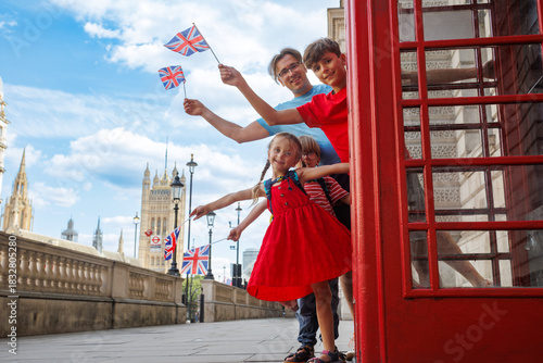 Happy family leans out of a red London booth, waving UK flags