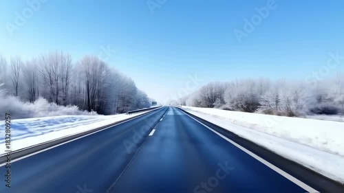 A snow-covered highway stretches ahead, bordered by frosted trees under a clear, bright blue sky