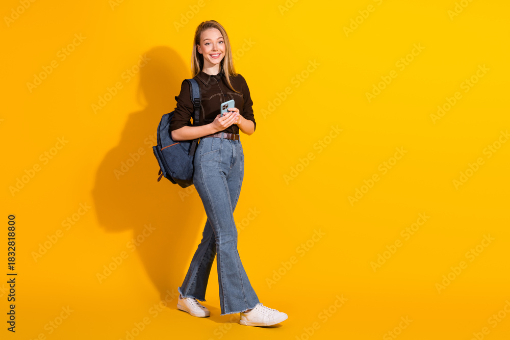 Naklejka premium Young female student with backpack walking against a bright yellow background smiling for fashion lifestyle stock photo