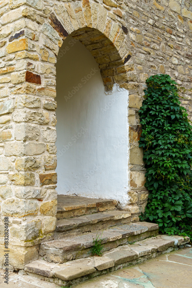Obraz premium close up of architectural details, old stone wall with arched opening and green ivy