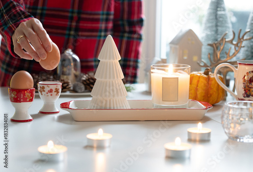 Candle light with Christmas decoration atmosphere while hand putting egg into the egg cup, with festive ambiance decorated on table.