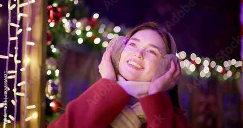 A young beautiful girl in a red coat walks in the evening at the European Christmas Market against the backdrop of illuminations and garlands.