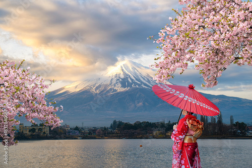 A beautiful Japanese girl in a kimono holding an umbrella, with Mount Fuji on the lakeside in the background and cherry blossoms in full bloom in spring.