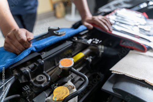 A close-up view of a young man holding a wrench as he checks and maintains his car engine by himself.