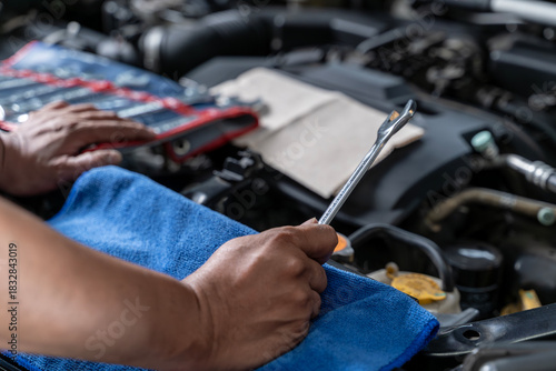 A close-up view of a young man holding a wrench as he checks and maintains his car engine by himself.