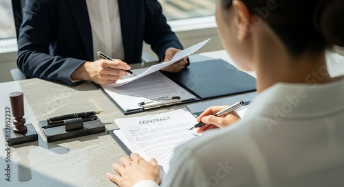 Professional business contract signing meeting with two people reviewing legal documents at marble desk with stamp and pens in modern office setting