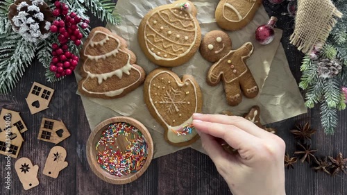 Festive gingerbread cookies are being decorated with sprinkles by hand on a rustic table
