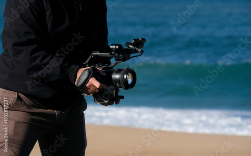Cameraman filming at the beach on a sunny day with a DSLR camera