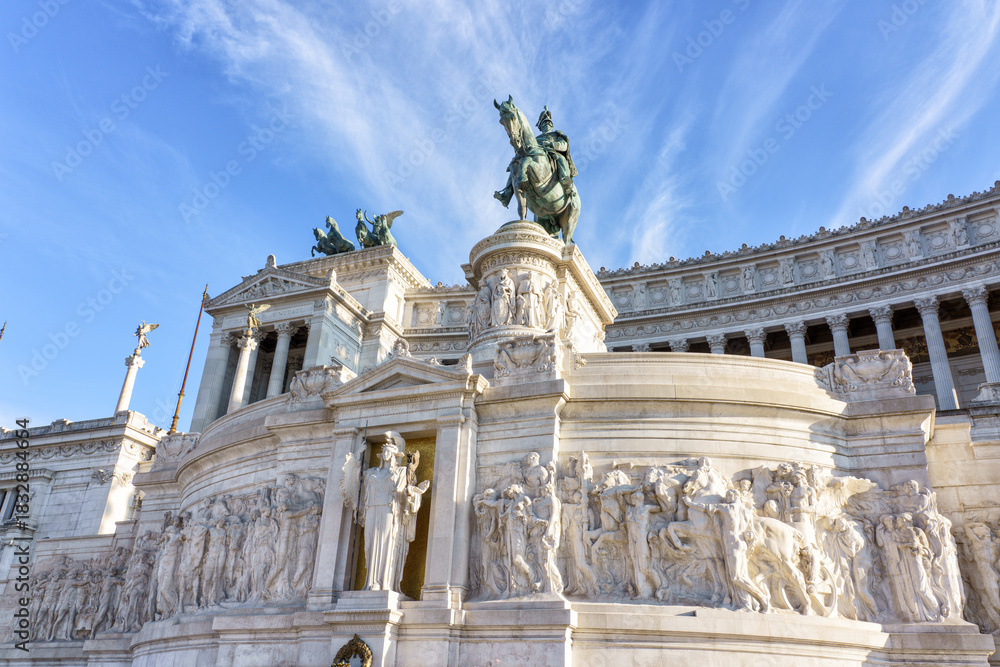 Fototapeta premium The Altare della Patria in Rome, Italy, featuring ornate marble sculptures, reliefs, and bronze quadriga statues on the monumental Victor Emmanuel II Memorial under a bright blue sky.