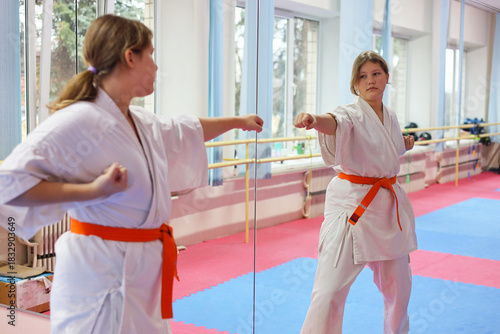 Sportive young girl wearing kimono doing exercises in large sports hall