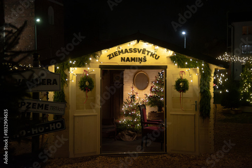 Valmiera,Latvia-November 30,2025-A cozy Christmas cabin decorated with wreaths, lights, and a glowing tree inside, inviting visitors with warm festive charm at night.
