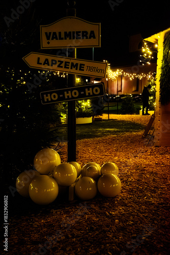Valmiera,Latvia-November 30,2025-Festive outdoor Christmas scene with decorative signposts, glowing lights, evergreen trees and white ornaments on a warmly lit pathway.
