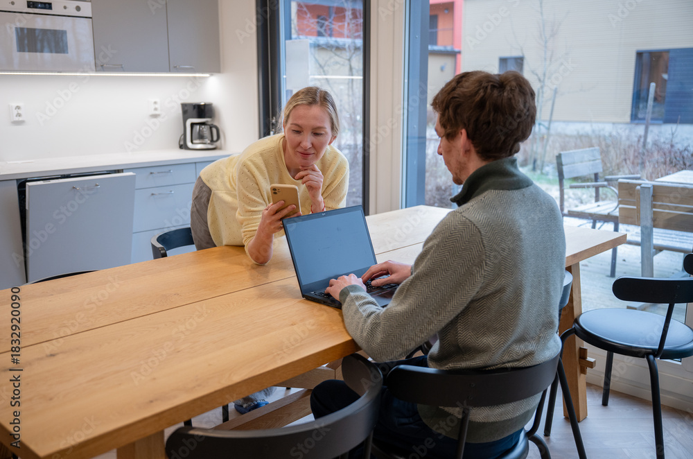 Obraz premium Woman showing smartphone to man working on laptop in modern kitchen