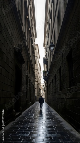 A lone figure strolls through a narrow, cobblestone alley in Barcelona. The buildings rise high on either side, and rainwater creates a reflective sheen on the ground, enhancing the serene atmosphere