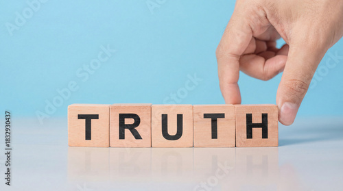 A hand places a wooden block with the letter h to complete the word truth on a table