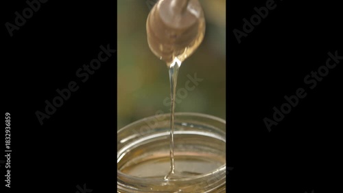 Natural Honey Pouring from Wooden Spoon into Jar
