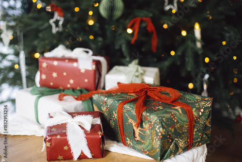 Stylish Christmas presents. Merry Christmas and Happy Holidays! Wrapped Christmas gift boxes on table at decorated xmas tree with lights. Atmospheric winter time